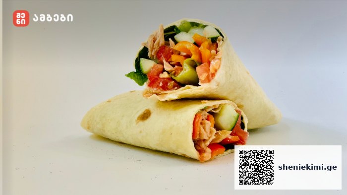Two fresh wraps filled with cucumber, tomatoes, peppers, greens and pink shredded protein, stacked on a white surface; red logo watermark in the upper-left corner.