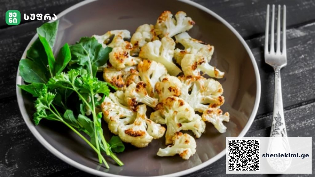 Plate of roasted cauliflower florets with a greens garnish on a dark wooden table, beside a decorative fork.