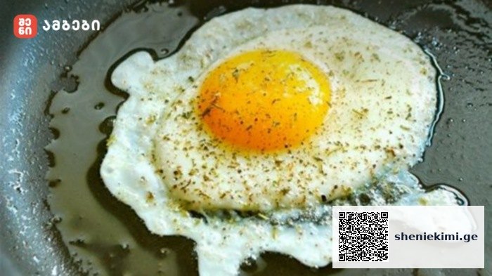 Sunny-side-up fried egg cooking in a skillet with herbs and oil around the edges.