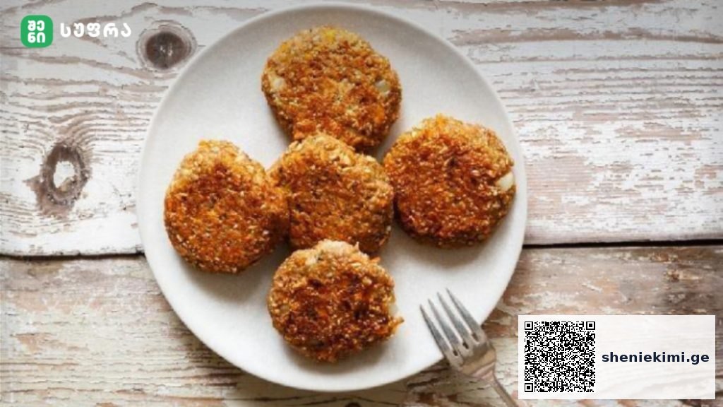 Five crispy breaded croquettes arranged on a white plate atop a rustic wooden table, with a fork nearby and a logo in the corner.