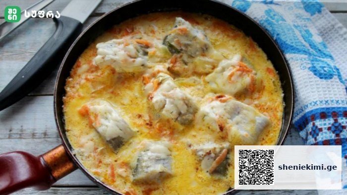 Skillet with chunks of white fish in a creamy yellow sauce with vegetables on a wooden table.