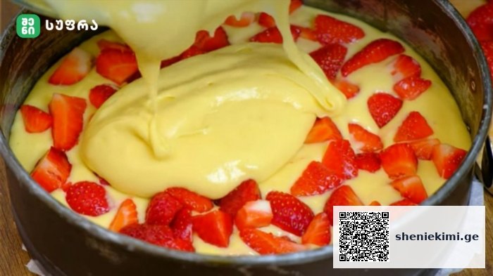 Cake batter is poured into a round baking pan surrounded by fresh strawberry slices, ready to bake.