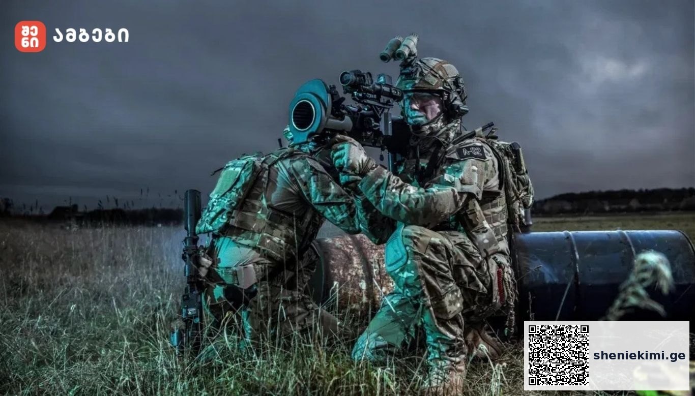 Two camouflaged soldiers kneel by a large artillery barrel in a grassy field at dusk, aiming through a scope outside the barrelled weapon