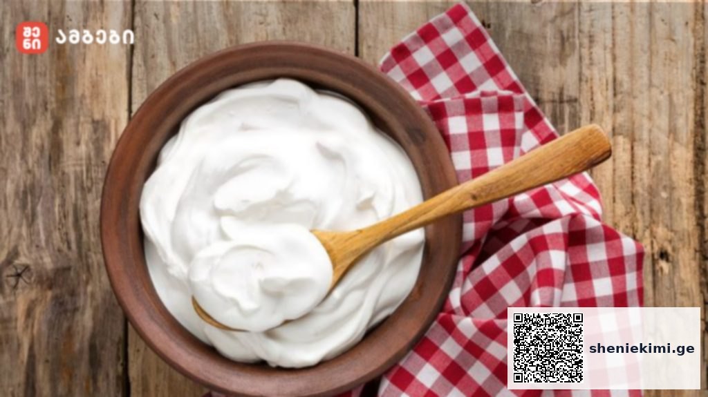 Bowl of creamy yogurt with a wooden spoon on a rustic wooden table, beside a red-and-white checkered napkin.