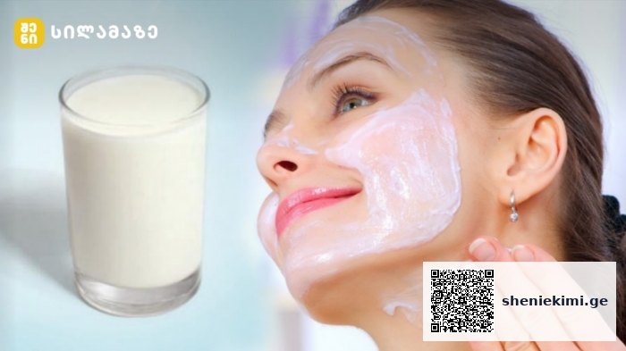 Woman smiles as she applies a white facial mask to her cheek, with a glass of milk visible to the left.