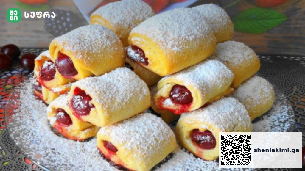 Rolls of yellow pastry filled with cherries, dusted with powdered sugar on a decorative platter