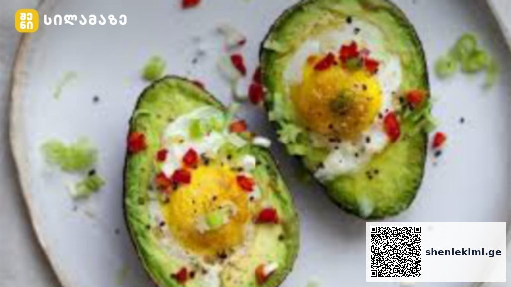 Two avocado halves hollowed and filled with boiled eggs, garnished with chopped greens and red pepper on a white plate.