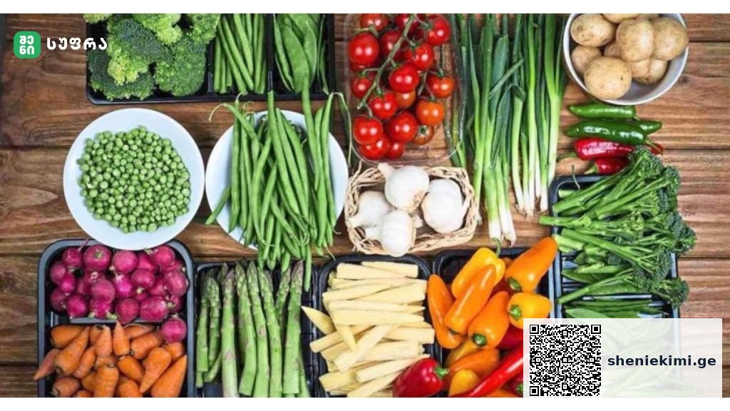 Wide assortment of fresh vegetables laid out on a wooden table, including broccoli, tomatoes, peppers, beans, carrots, and potatoes.