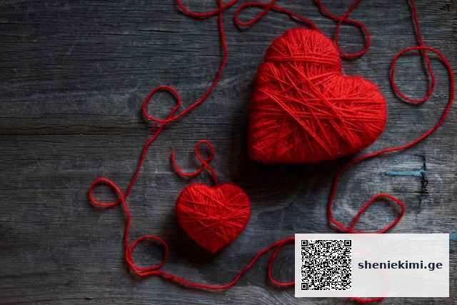 Two red yarn hearts on a dark wooden surface, with loose strands looping around them (Valentine's theme).