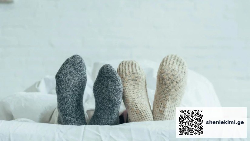 Person lying in bed with gray and beige knitted socks peeking out from under a white duvet.