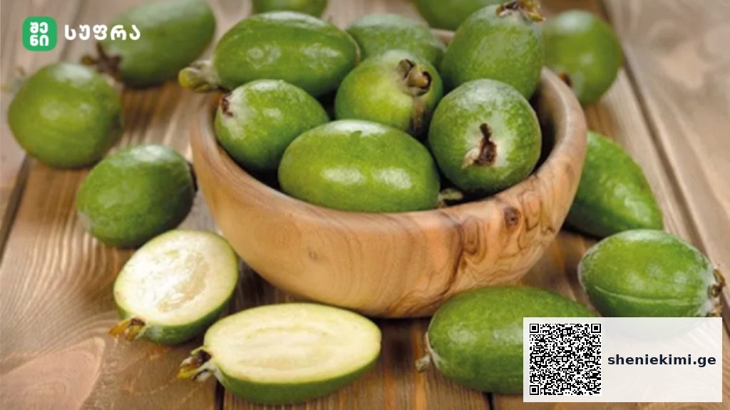 Green feijoa fruits in a wooden bowl on a rustic wooden table, one cut open to show pale flesh inside.