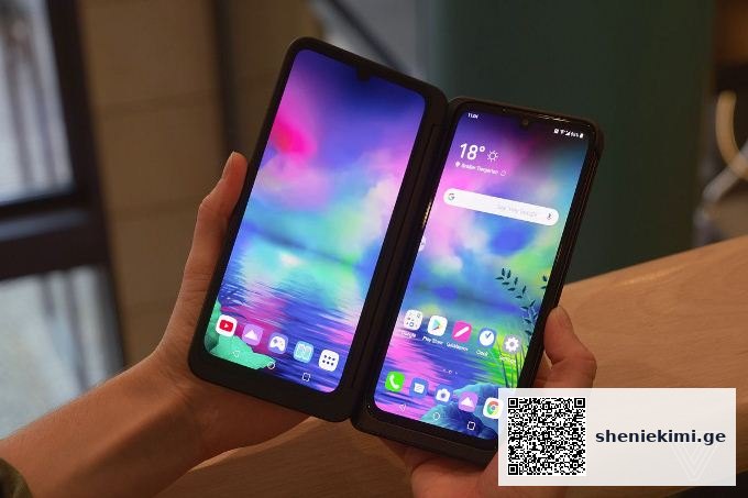 Two smartphones in a dual‑screen foldable case, held in each hand, displaying vibrant colorful home screens with app icons.