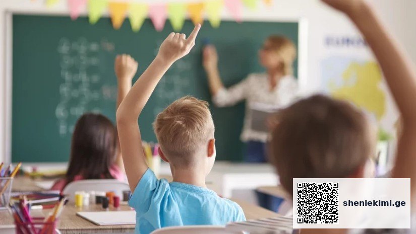 Classroom scene with a teacher at the chalkboard as students raise their hands to answer a question, colorful bunting overhead.