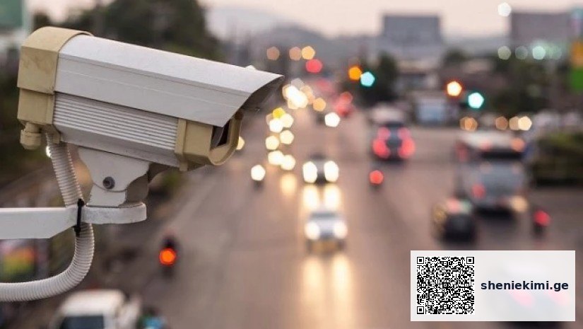 Surveillance camera overlooking a busy multi-lane highway with blurred car lights at dusk.