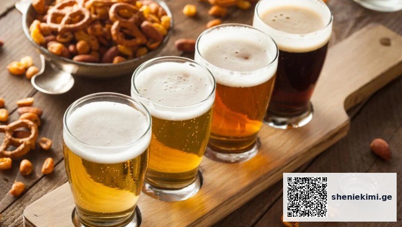 Four beers in a flight lined up on a wooden board with pretzels and nuts nearby, ready for tasting.