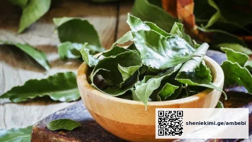 Fresh bay leaves in a wooden bowl resting on a rustic wooden surface.
