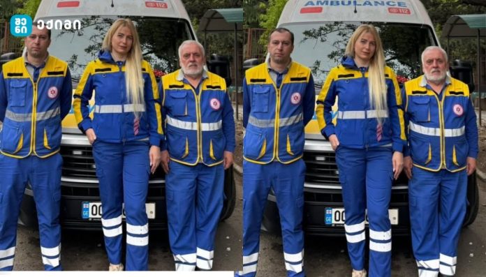 Three emergency medical workers in blue and yellow uniforms with reflective stripes stand in front of an ambulance showing 112 on the hood.