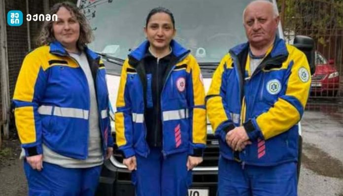 Three emergency responders in blue and yellow uniforms standing in front of a van.