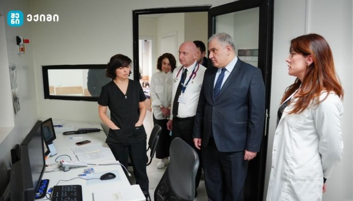 Healthcare professionals in a small clinic office, standing by a desk with computers and paperwork as they discuss.