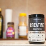 Tub of Creatine Monohydrate supplement on a shelf, foreground in focus with blurred background bottles.