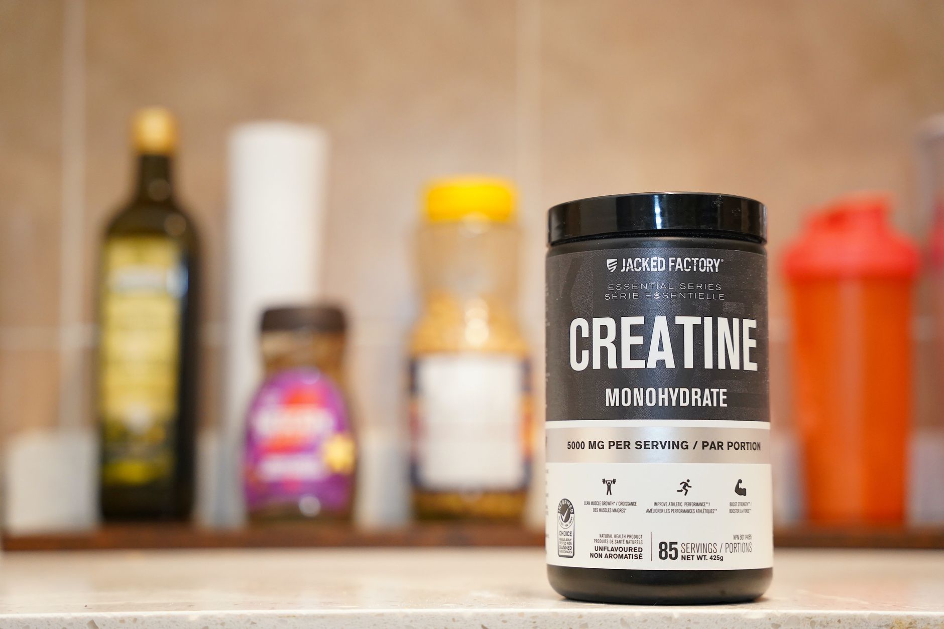 Tub of Creatine Monohydrate supplement on a shelf, foreground in focus with blurred background bottles.
