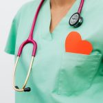 Healthcare worker in green scrubs with a stethoscope and an orange heart in the chest pocket