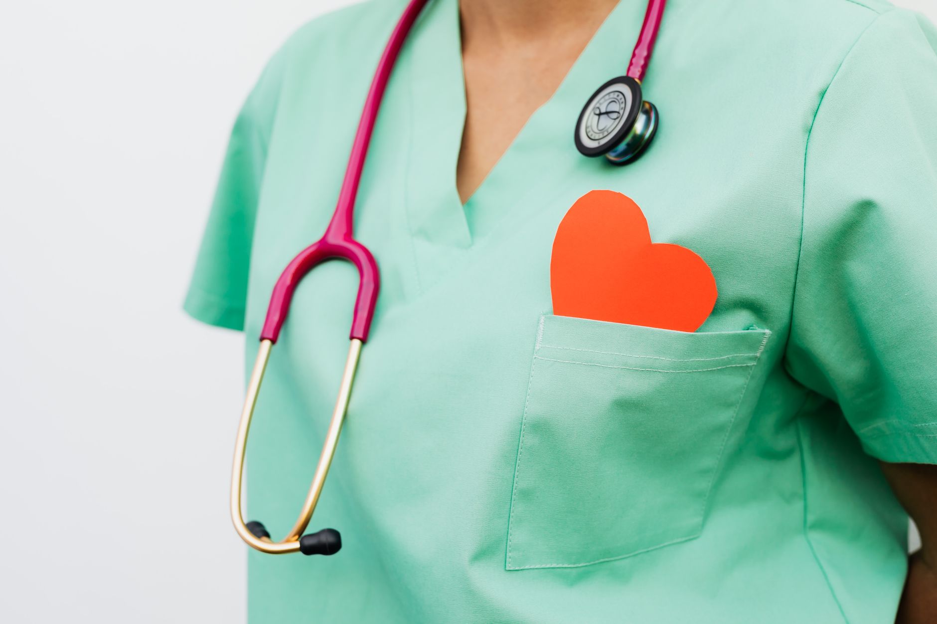 Healthcare worker in green scrubs with a stethoscope and an orange heart in the chest pocket